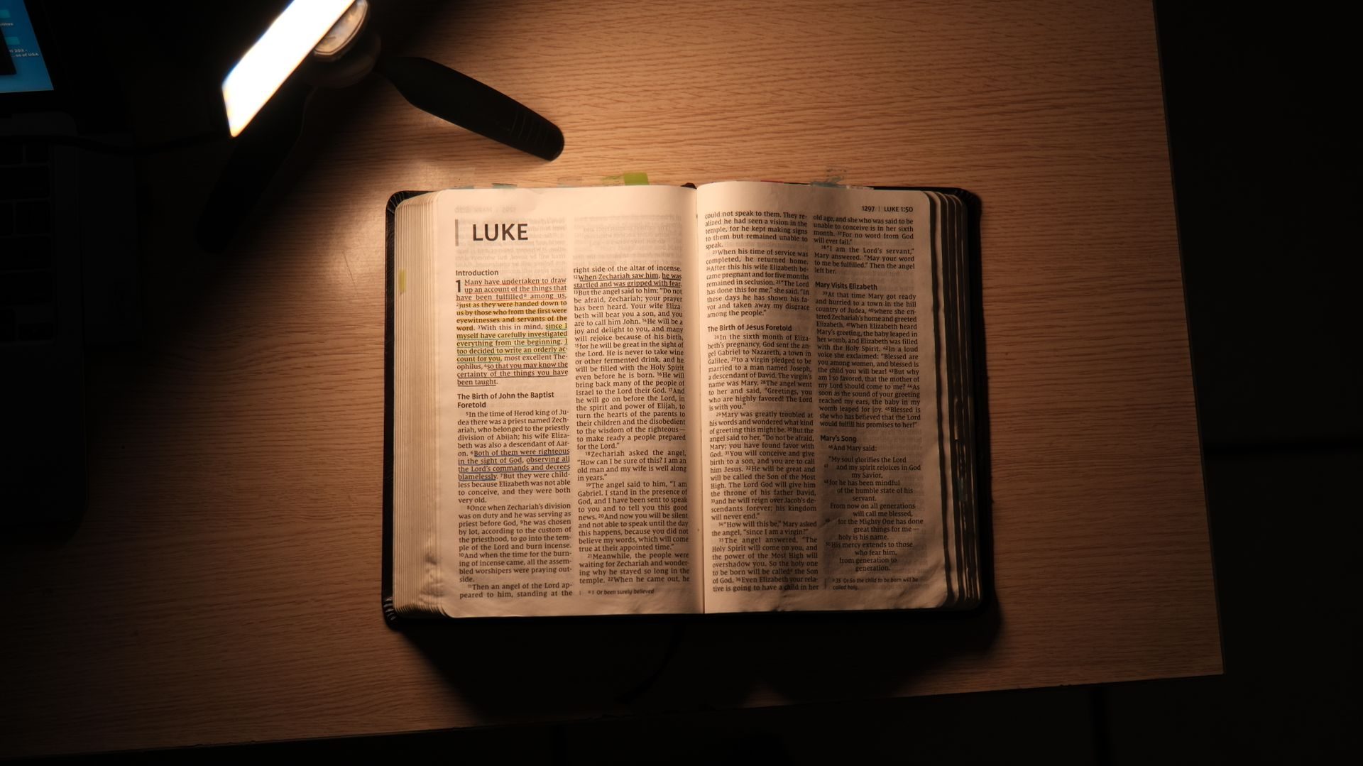 An open Bible on a wooden desk, lit by a warm reading lamp